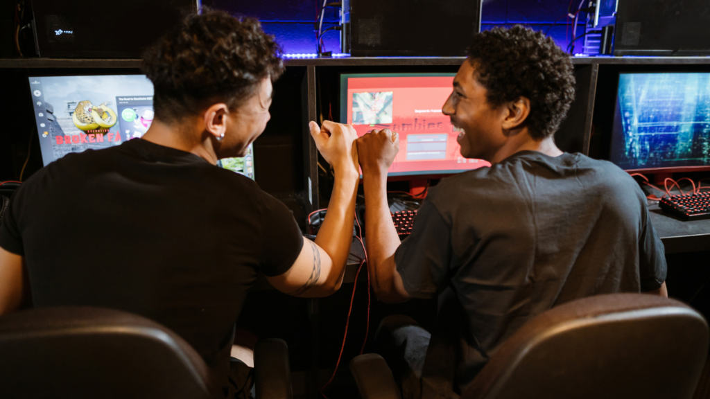 Two teen boys fist-bumping in front of gaming PCs
