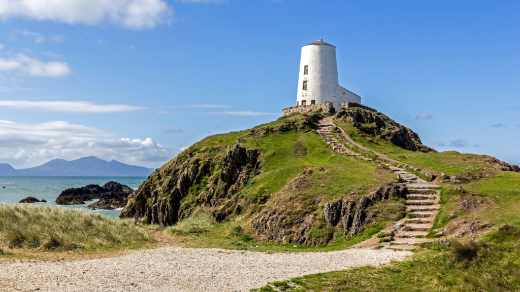White lighthouse atop of a rocky and grassy hill
harddwch