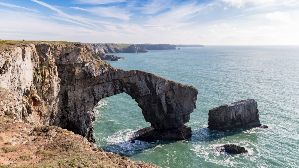 Rugged coastal cliff with a rock formation arch in the blue sea - Pembrokeshire Coast