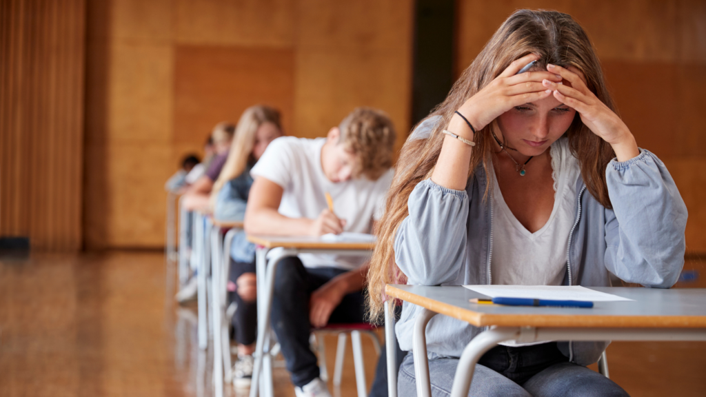Young people in exam hall with girl holding her head in hands
