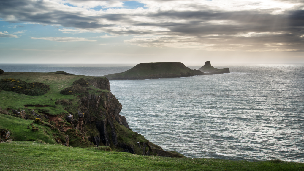 Steep cliff face in the foreground with island in the background - Worm's Head, Rhosilli - great walks in Wales