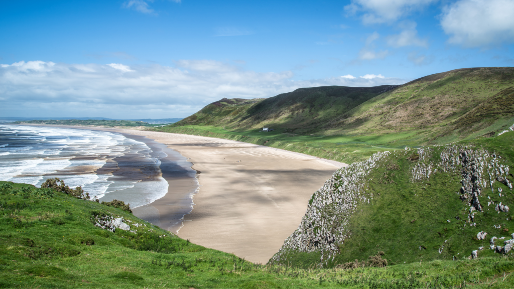 Blue and white waves hitting a sandy beach shoreline, with grassy cliffs